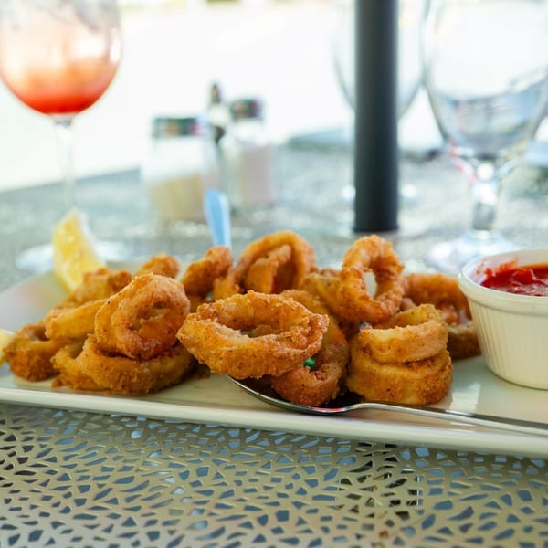 Crispy fried calamari with a lemon wedge and red dipping sauce on a white plate at Bazzarelli.