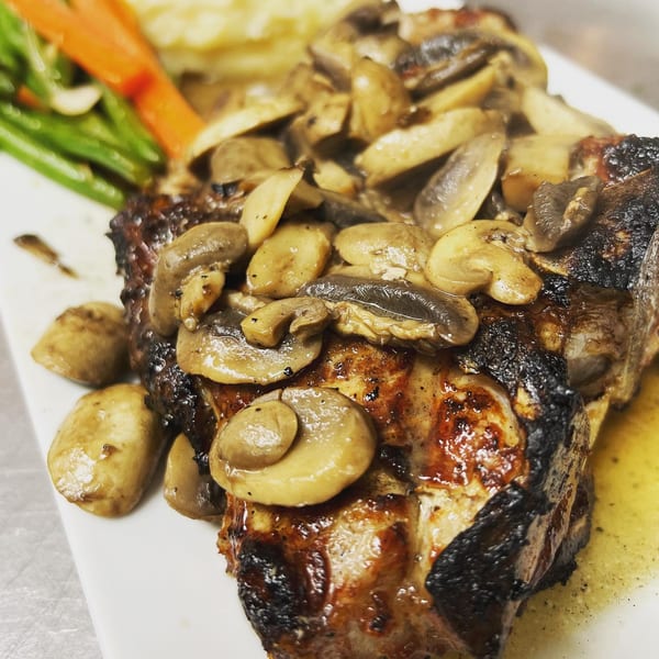 Grilled steak topped with sautéed mushrooms, served with green beans and carrots.