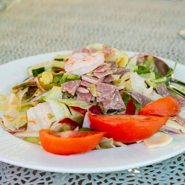 A Bazzarelli Italian salad with lettuce, tomatoes, meats, and shrimp on a white plate.